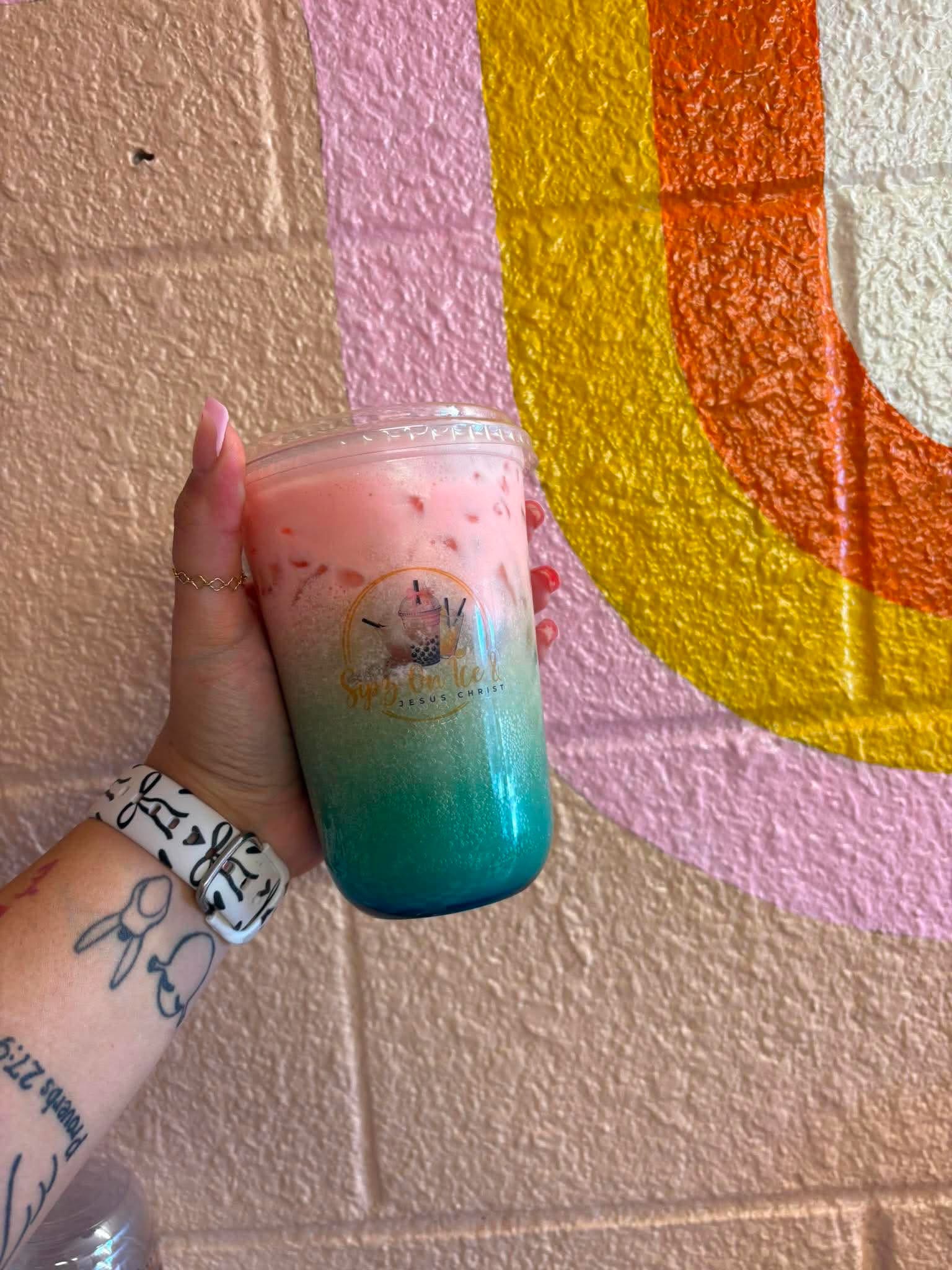 Pink to teal ombre drink held up against a colorful mural