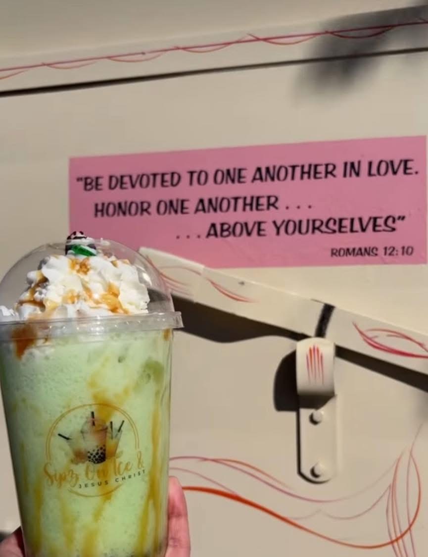 A Sipz On Ice drink held up against the trailer, featuring a Romans 12:10 scripture decal